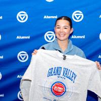 Young women holding up her crewneck and smiling in front of photo backdrop